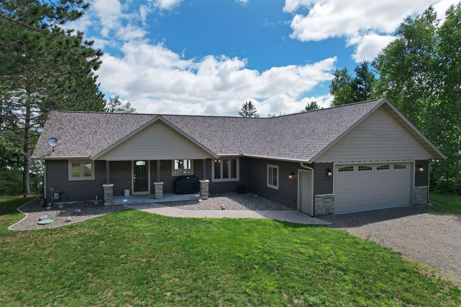 Tan and gray house with a stone facade, garage, and porch; set against green lawn and trees.