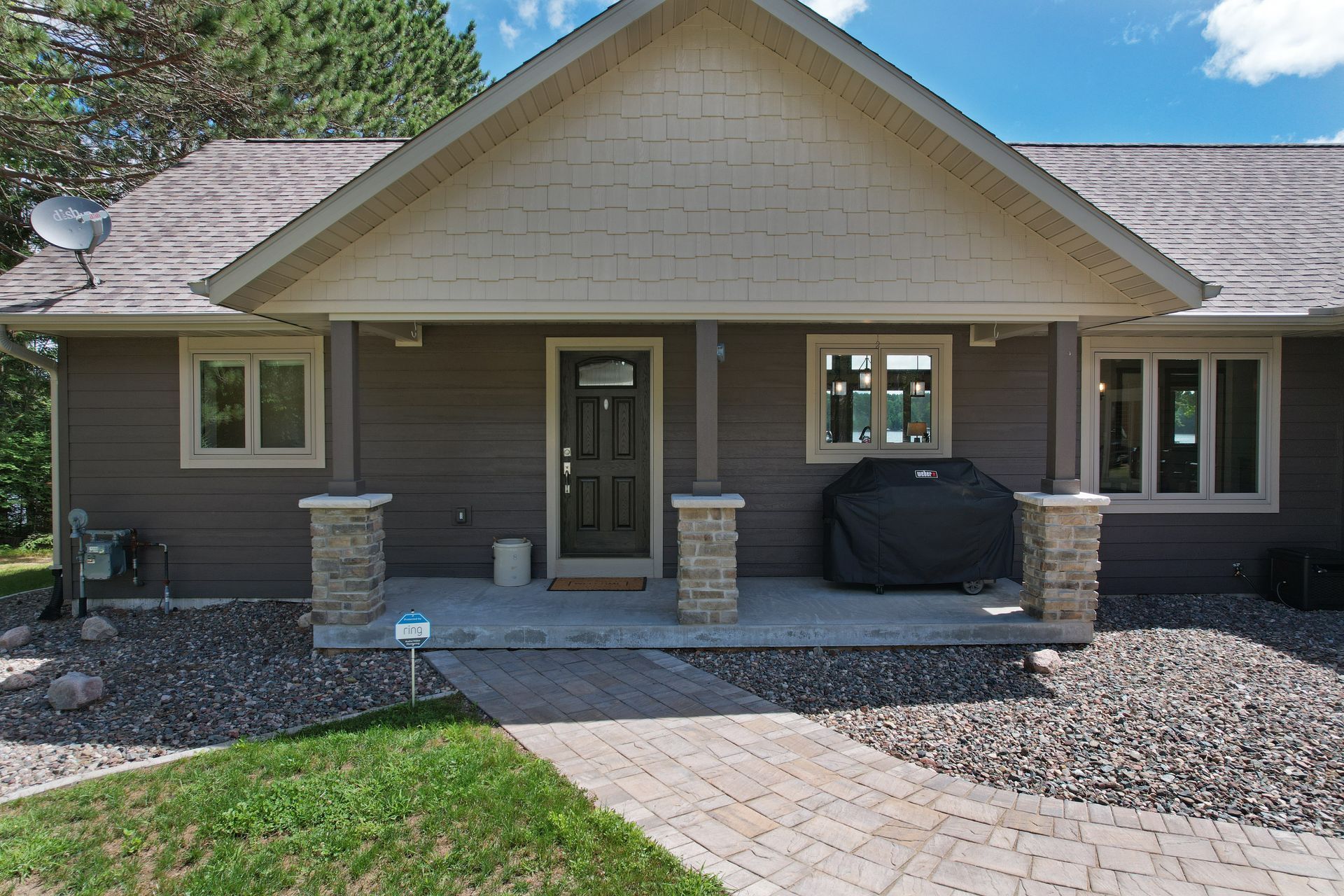 Brown house exterior with a covered porch and stone columns; paved walkway leads to front door.