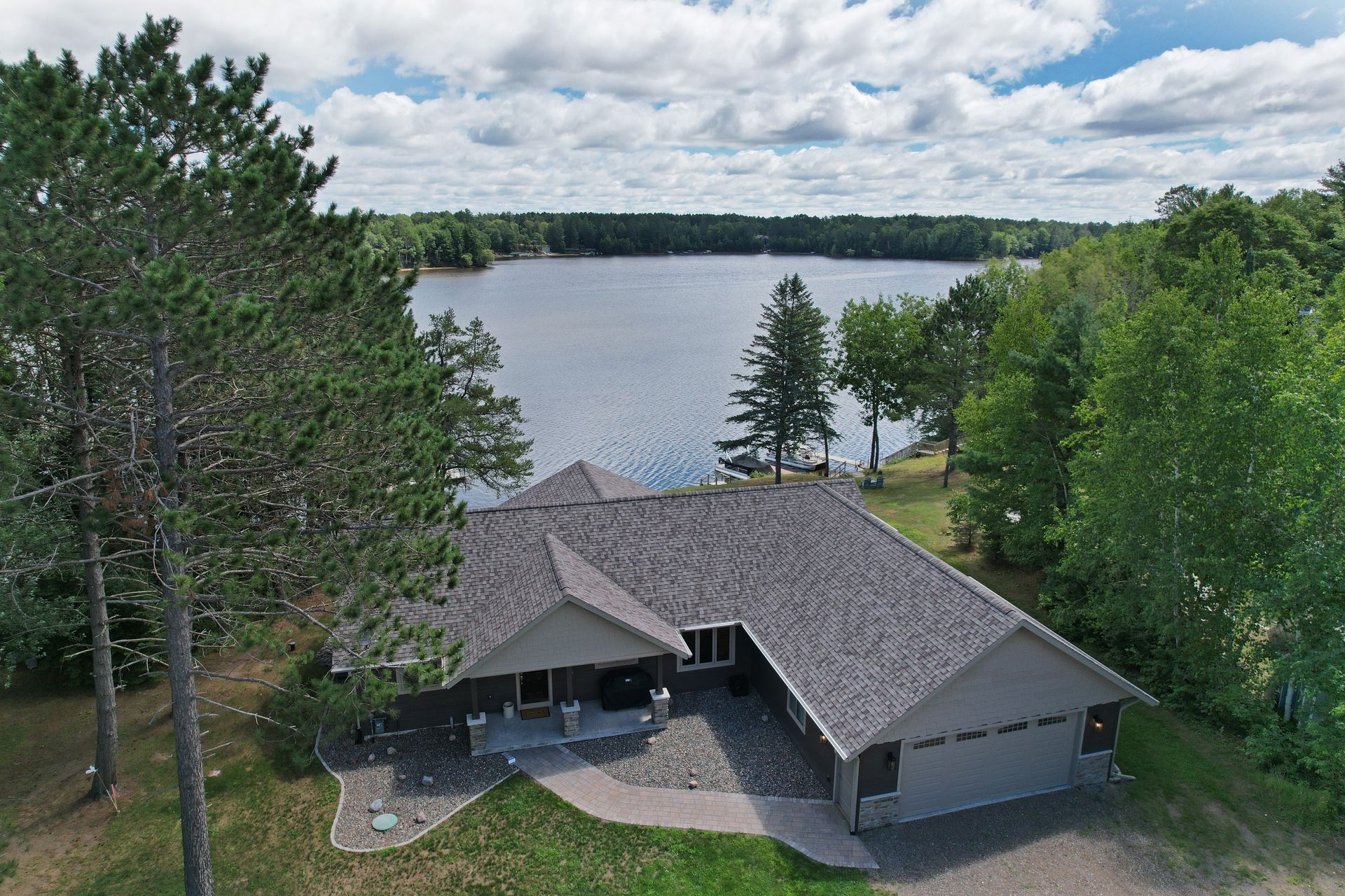 A house with a dark roof on a lake with trees. Cloudy sky.