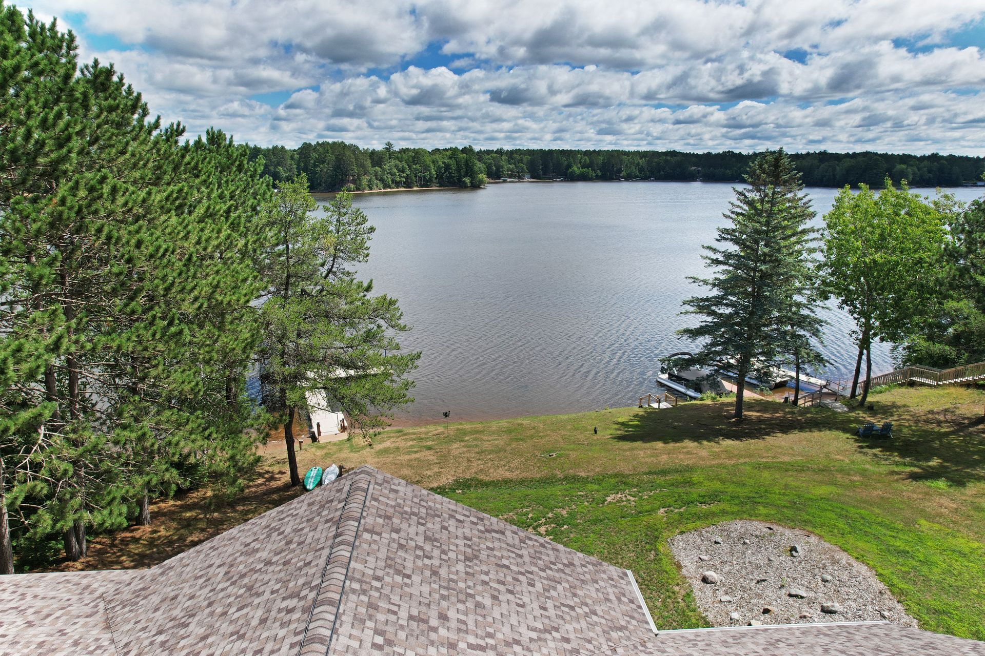 Lake view from rooftop with trees, blue sky, and clouds.