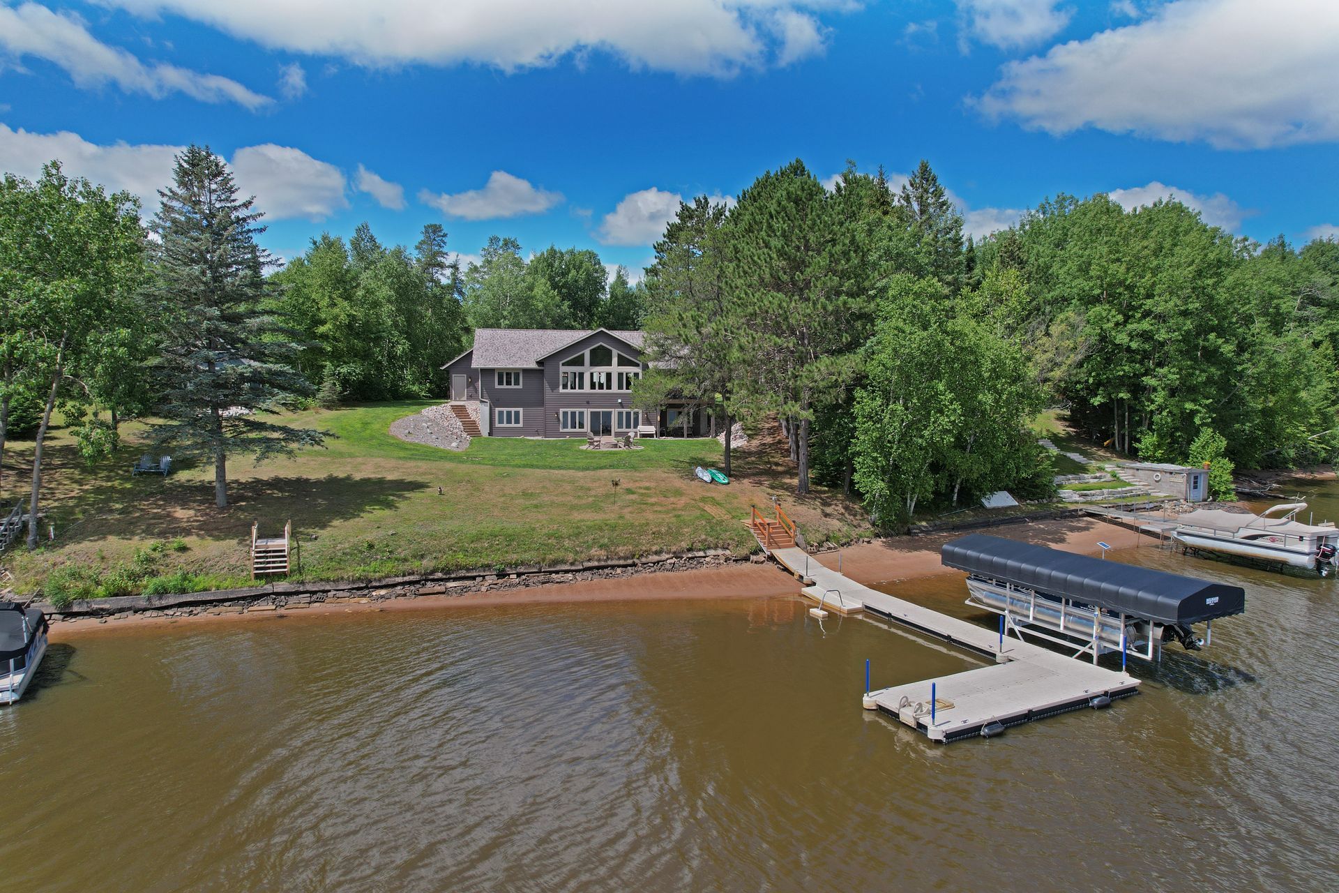 Lakefront house with dock and boat lift under a blue sky.
