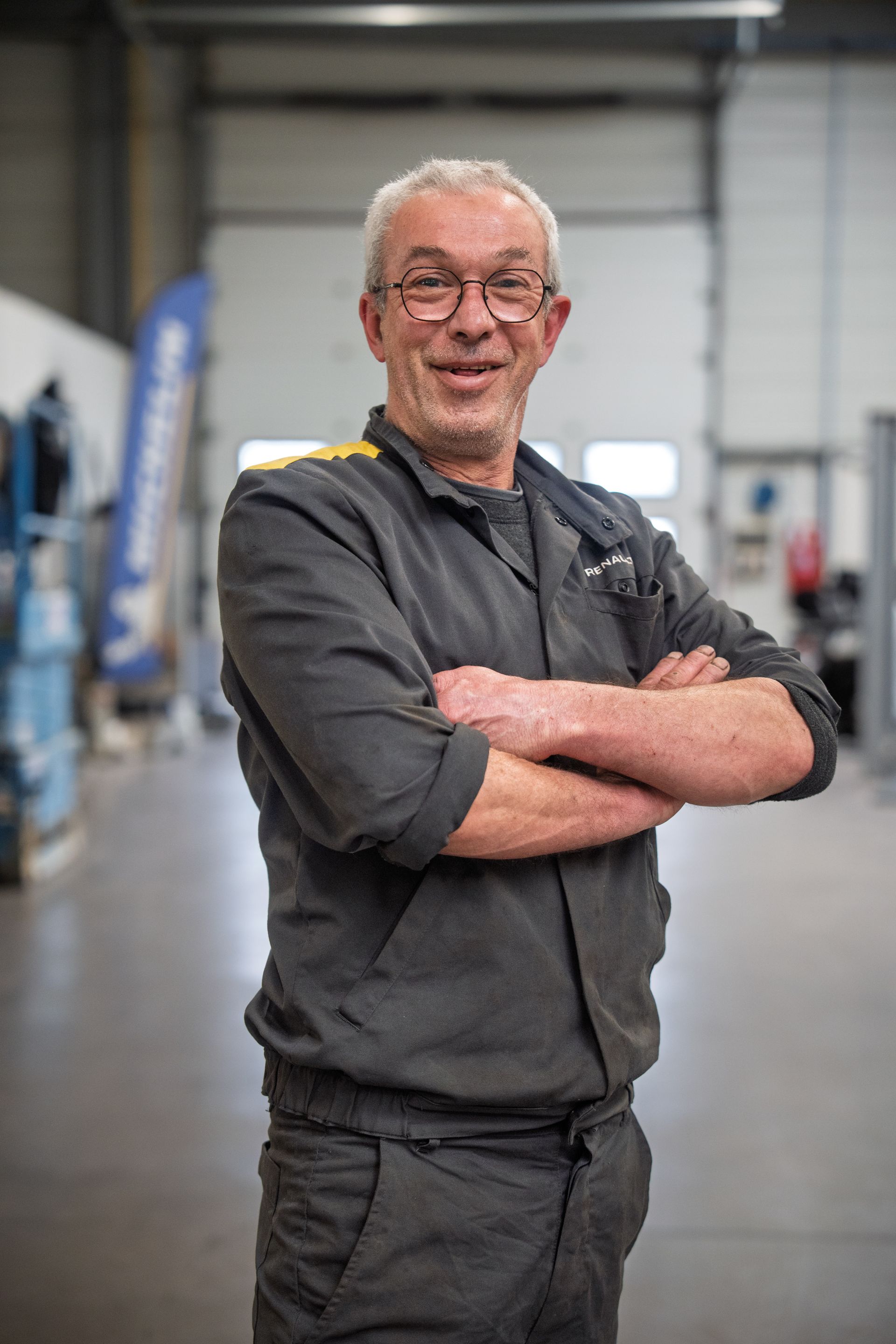 Homme avec les cheveux blancs et des lunettes vêtu d'une chemise noire et croisant les bras