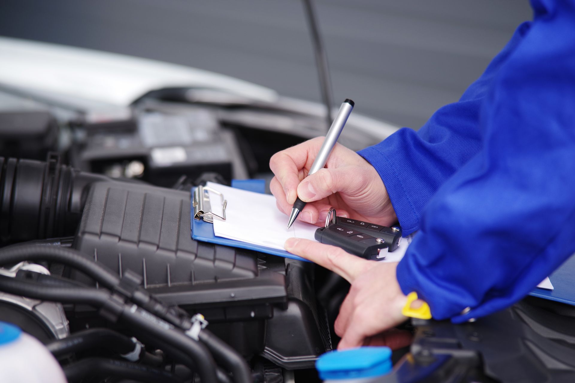 Main d'homme prenant des notes avec, comme support, le compartiment moteur d'une voiture