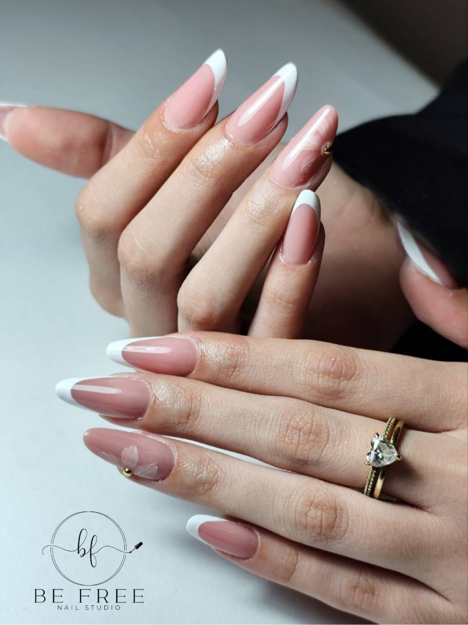 Mani con unghie laccate color rosa nude e anelli d'oro appoggiate insieme su una superficie chiara.