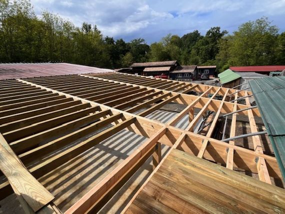 Toiture en construction avec charpente apparente en bois et panneaux métalliques ondulés sous un ciel bleu