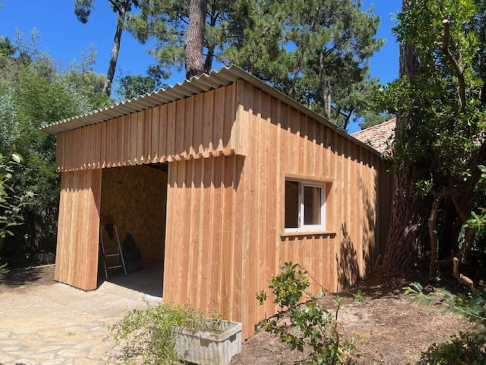 Petit abri en bois avec façade ouverte dans une cour boisée et ensoleillée
