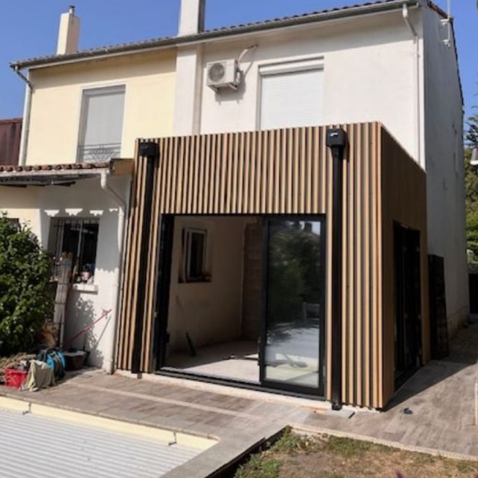 Maison à deux étages avec une extension de patio moderne en lattes de bois et des portes coulissantes en verre