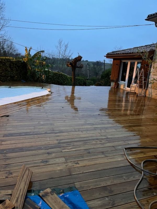 Terrasse en bois trempée par la pluie, à côté d'une piscine et d'une maison.