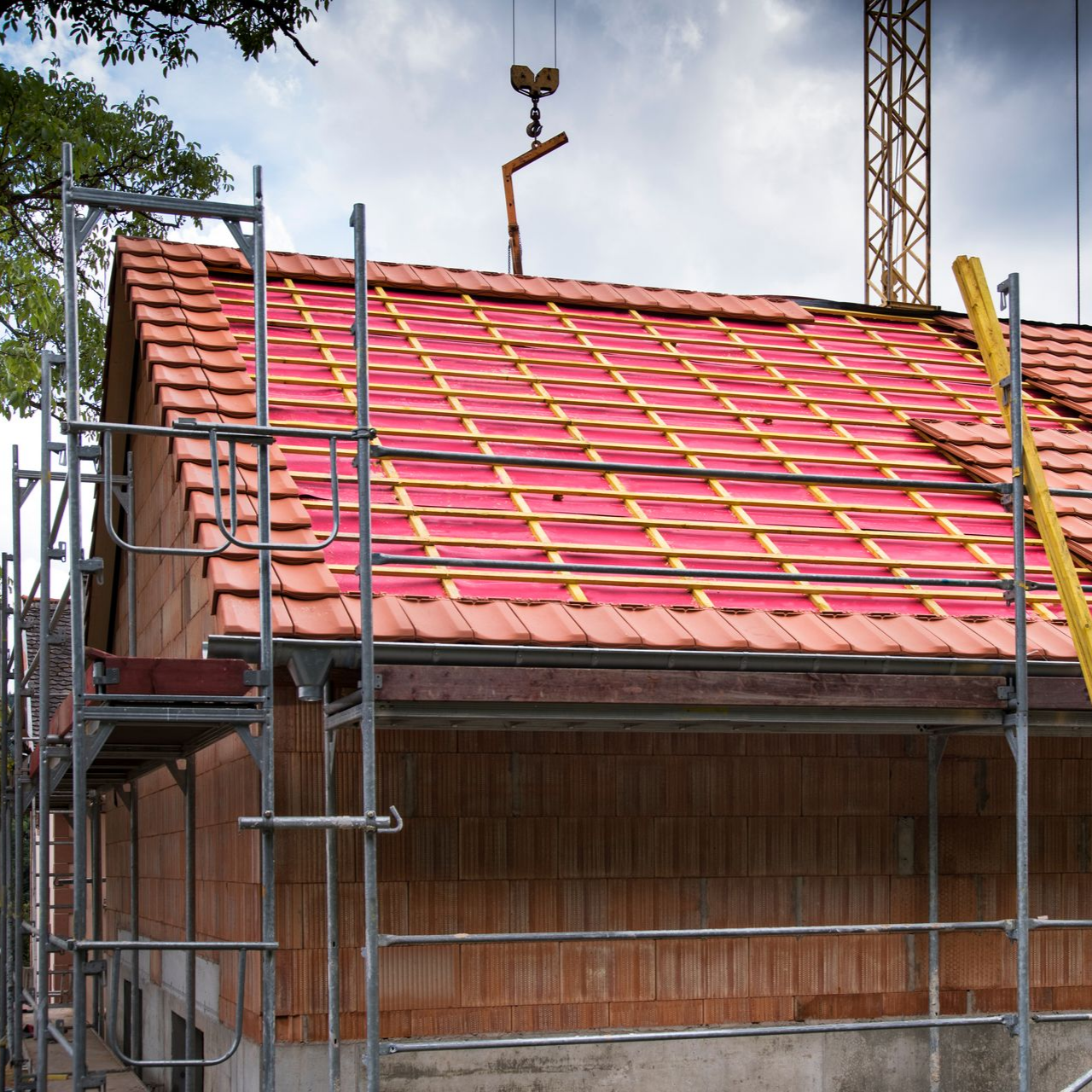 Toiture en construction avec tuiles rouges, liteaux jaunes et échafaudages sur un bâtiment en bois.