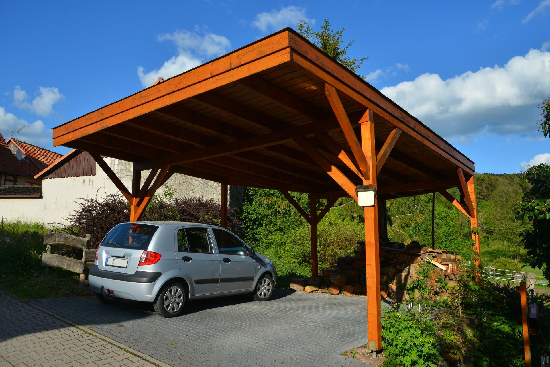 Voiture grise garée sous un abri en bois dans une allée.