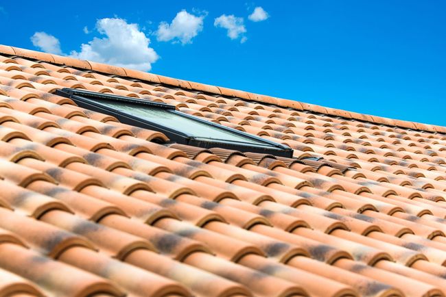 Toit en tuiles de terre cuite orange avec une lucarne sous un ciel bleu