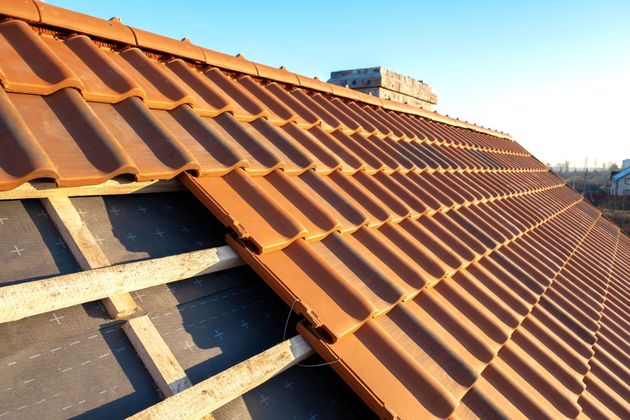 Gros plan sur un toit de tuiles rouges en construction, avec des liteaux en bois apparents, sous un ciel bleu.