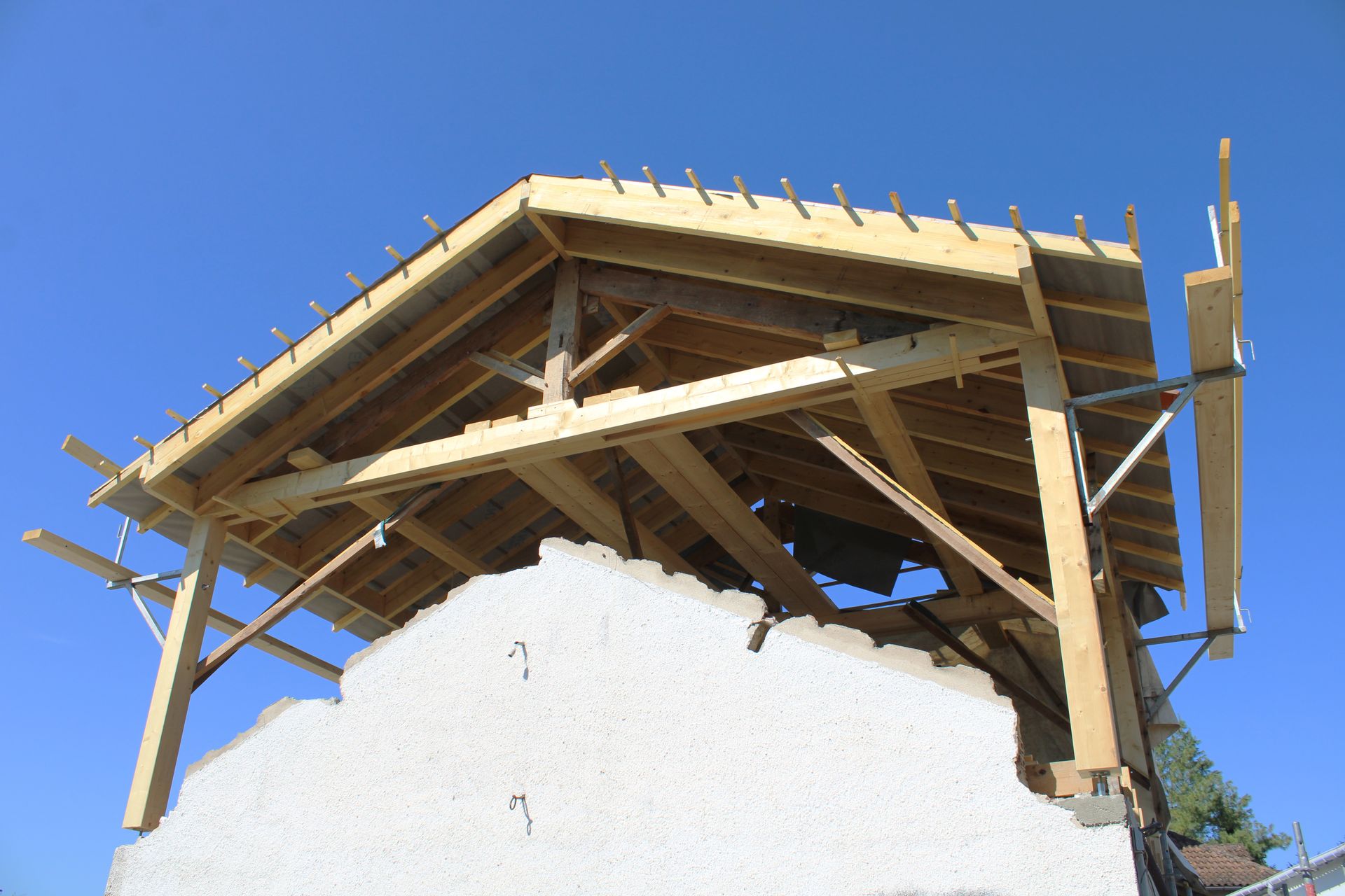 Charpente de toit en bois partiellement construite sur une structure blanche se détachant sur un ciel bleu clair