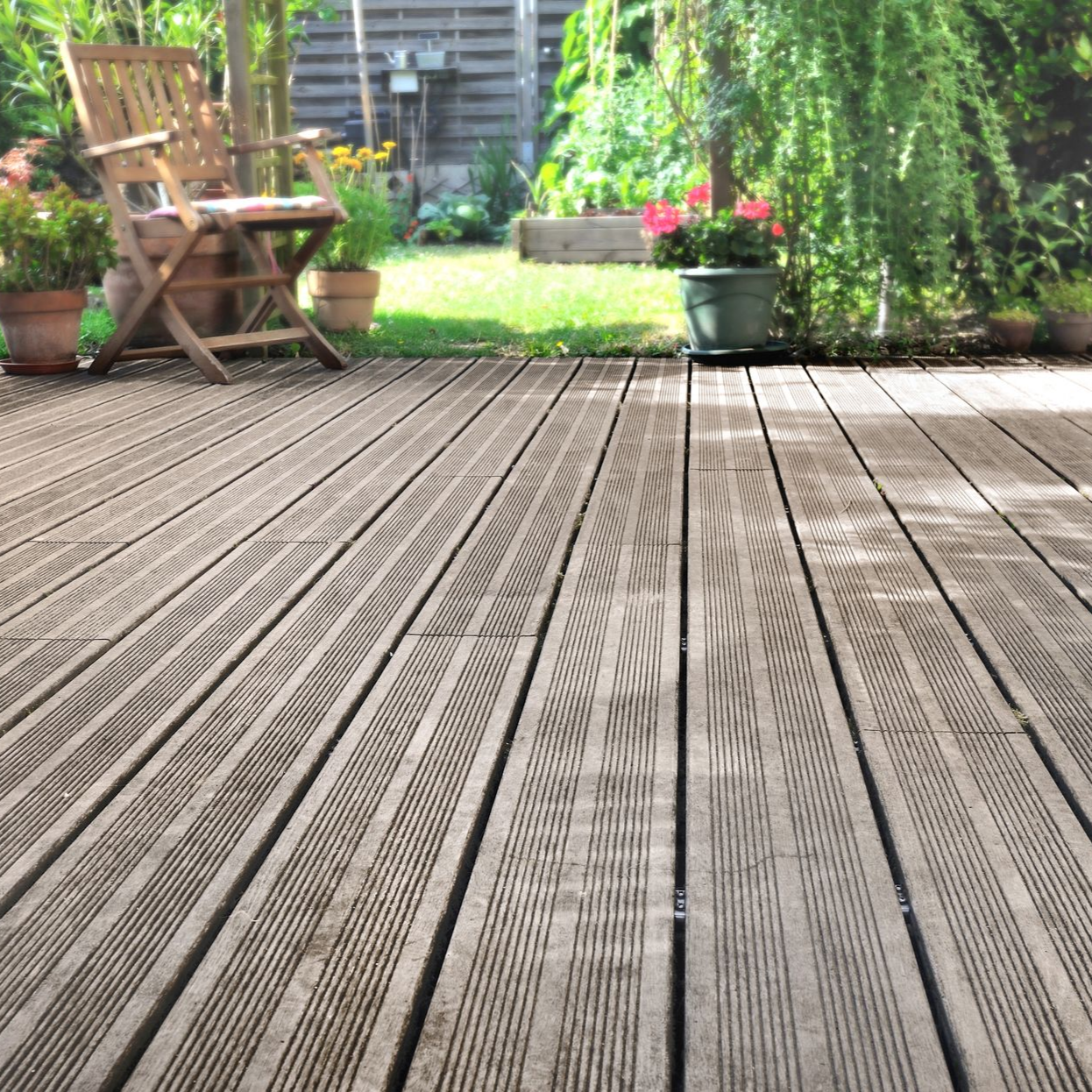 Terrasse en bois donnant sur un patio de jardin avec une chaise, des fleurs en pot et une végétation luxuriante.