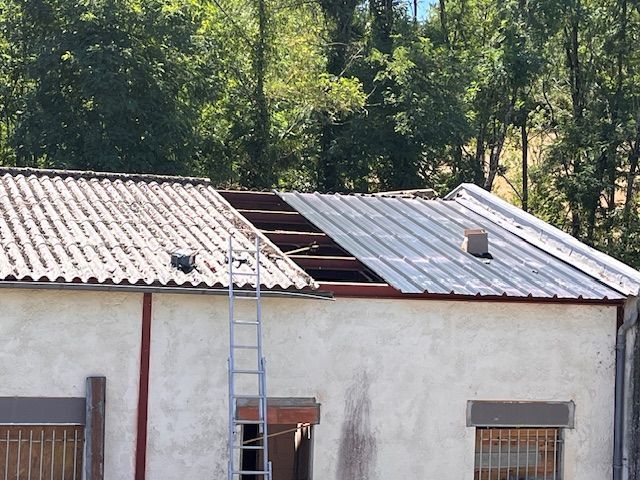 Toiture en tôle rouillée en cours de réparation à l'aide d'une échelle appuyée contre un bâtiment blanc, arbres en arrière-plan
