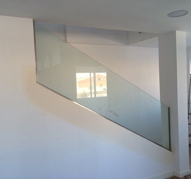 Una escalera con barandilla de cristal y una ventana al fondo.