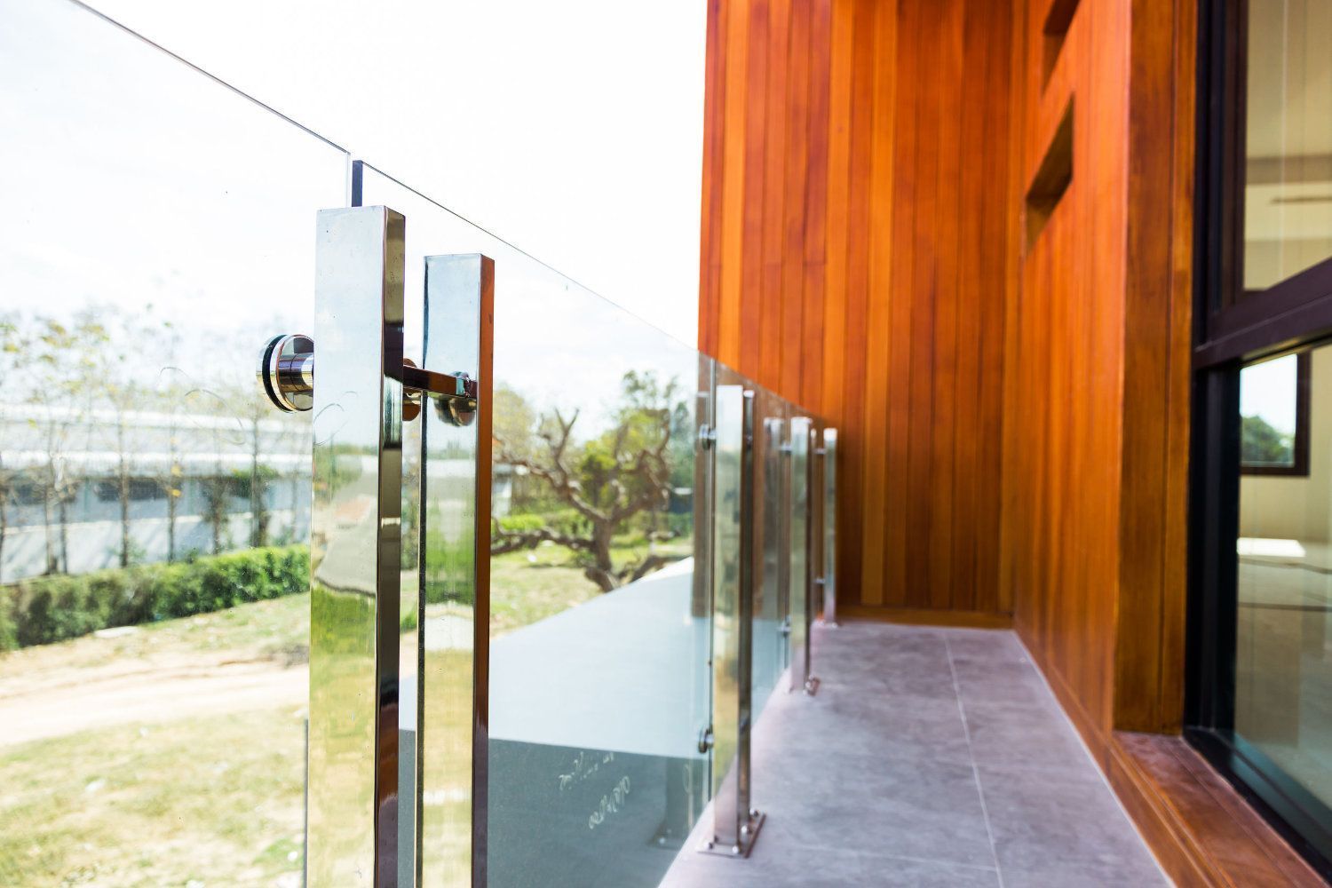 Un balcón con barandilla de cristal y pared de madera.