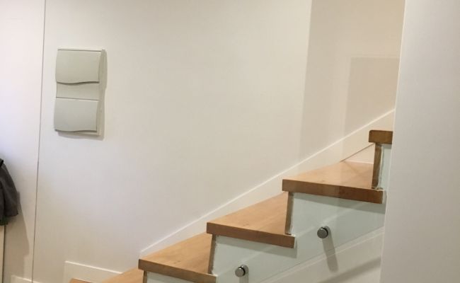 Una escalera con escalones de madera y barandilla de cristal en una habitación.