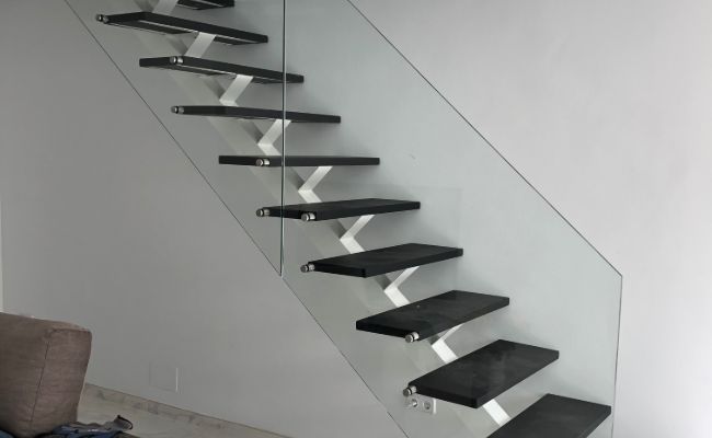 Una escalera con escalones negros y barandilla de cristal en una sala de estar.