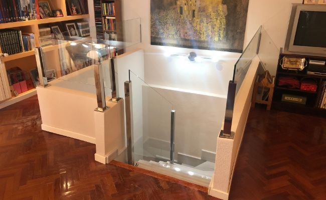 Una sala de estar con barandilla de vidrio y escaleras que conducen al segundo piso.