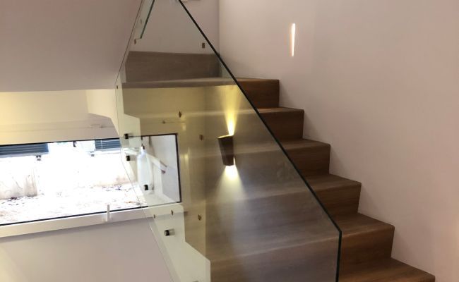 Una escalera con barandilla de cristal y una ventana.