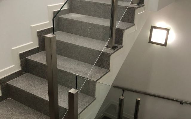 Una escalera con barandilla de cristal y una luz en la pared.