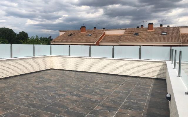 Un balcón con barandilla de cristal y suelo de baldosas.