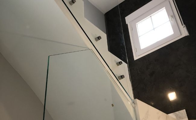 Una escalera con barandilla de cristal y una ventana.