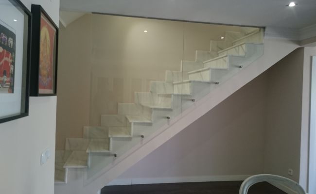 Una escalera blanca con barandilla de cristal en una habitación.