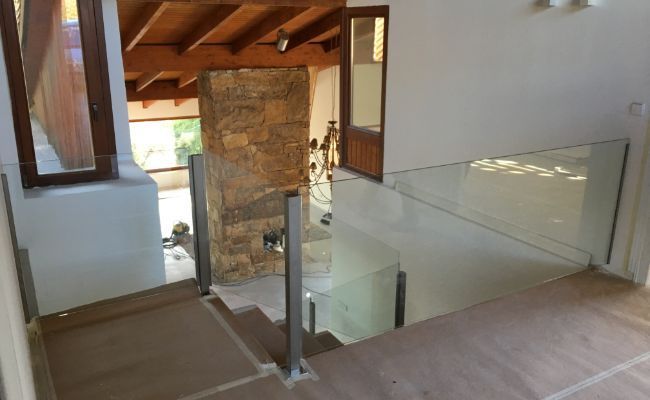 Una escalera con barandilla de cristal y una chimenea al fondo.