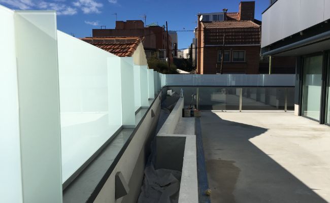 Un balcón con barandilla de cristal y un edificio de ladrillo al fondo.