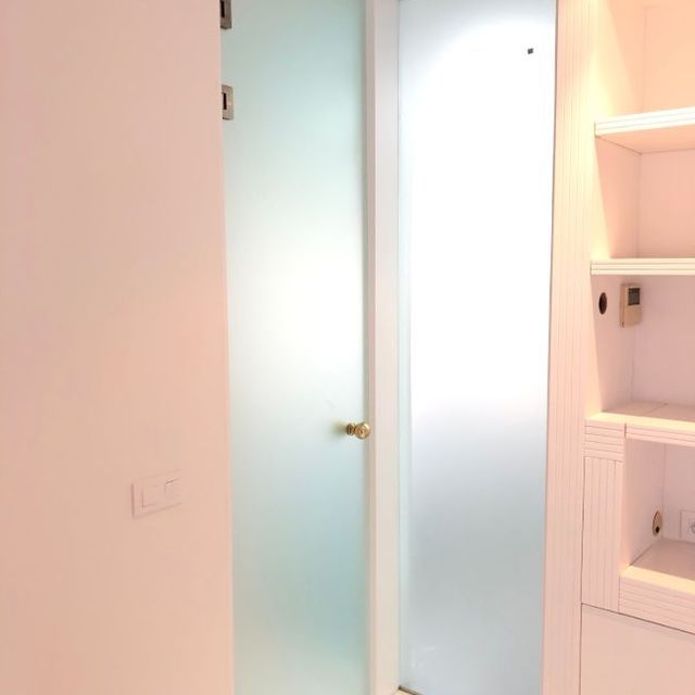 Un baño con puerta de vidrio esmerilado y estantes.