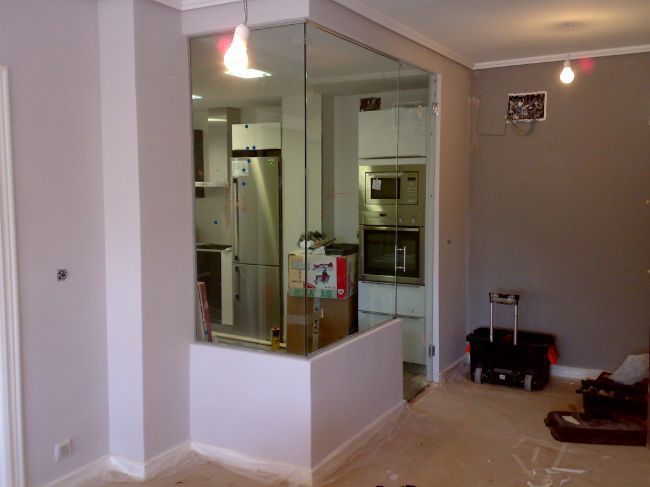 Una habitación con una pared de vidrio entre ella y una cocina.