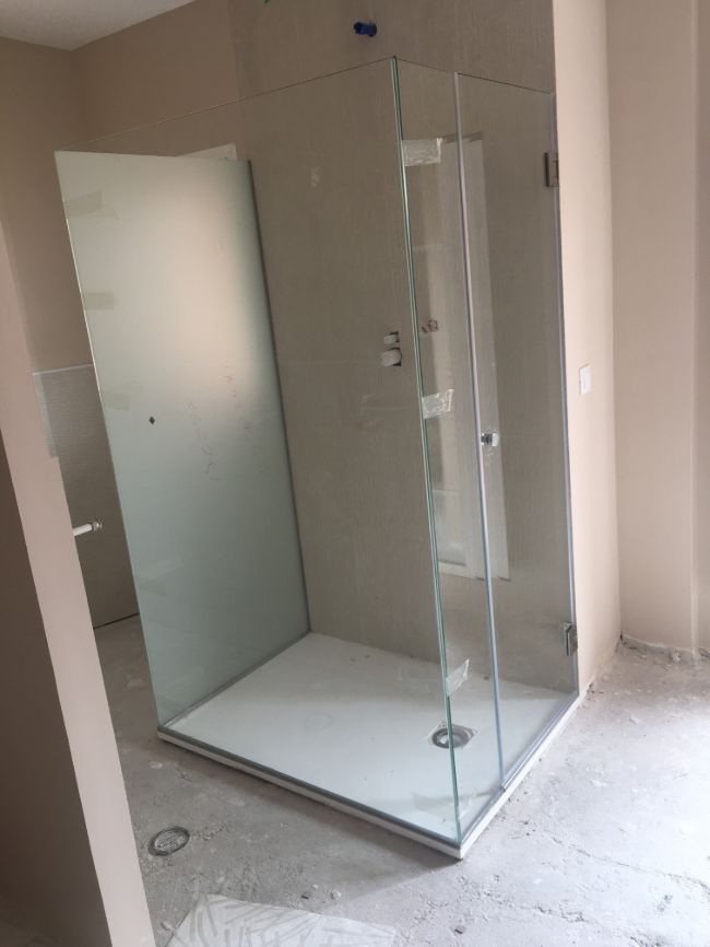 Un baño con ducha a ras de suelo y puerta de cristal.