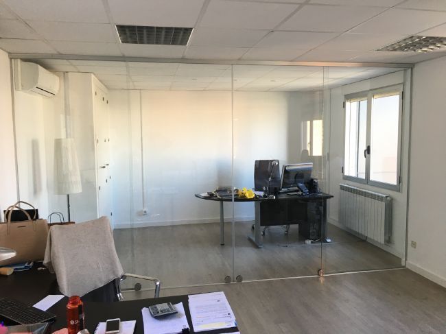 Una oficina con un escritorio y sillas y una pared de vidrio.