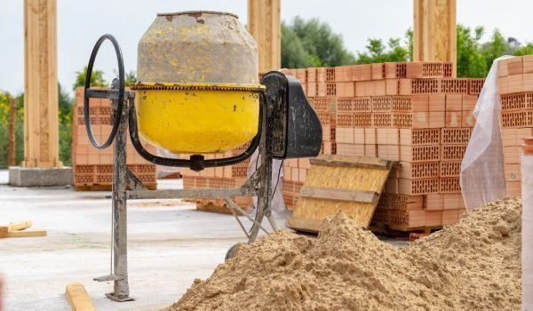 Una hormigonera amarilla está junto a una pila de arena en un sitio de construcción.