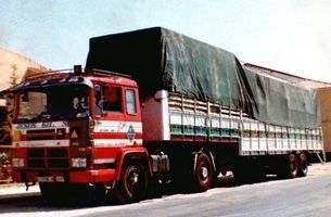 Un camión rojo y blanco con una lona verde encima está estacionado al costado de la carretera.