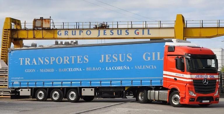 Un camión rojo y azul está estacionado debajo de una grúa que dice grupo jesus gil