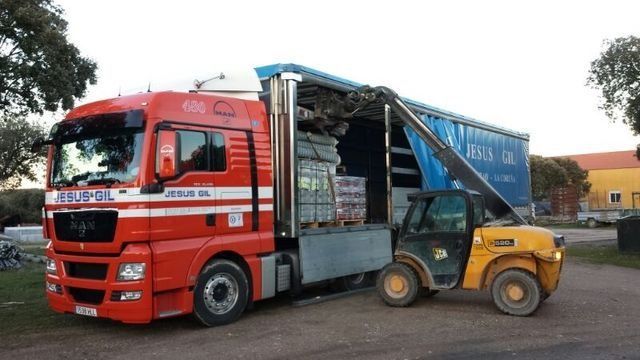 Un camión rojo con una lona azul está siendo cargado por una carretilla elevadora.