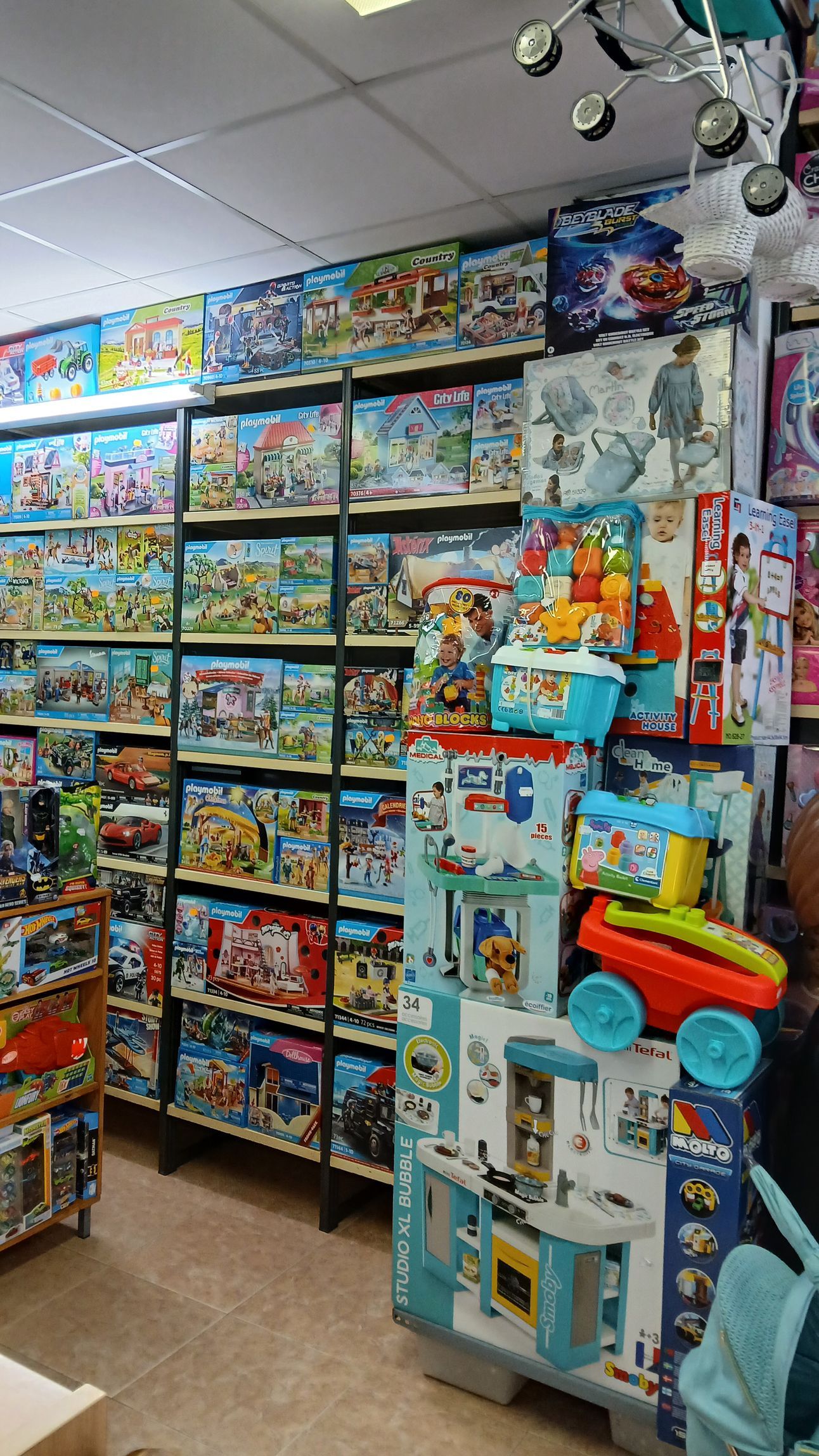 Pasillo de juguetería con estantes repletos de coloridas cajas de juguetes y juegos apilados bajo luces brillantes.