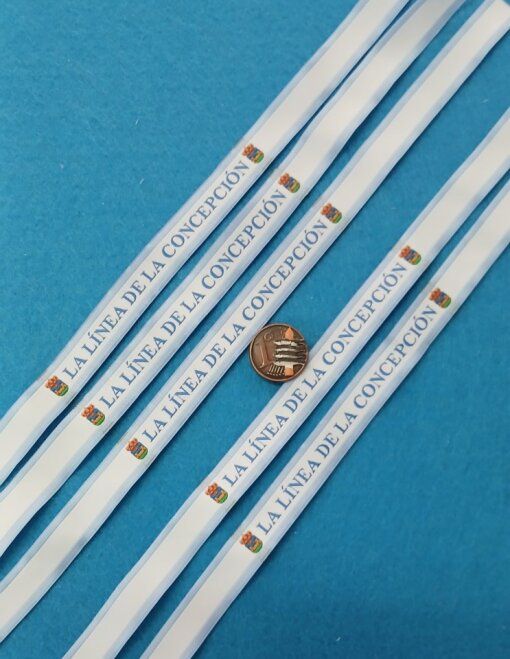 Cordones de marca en azul y blanco con el texto “La Línea de la Concepción” y una pequeña moneda sobre fondo azul.