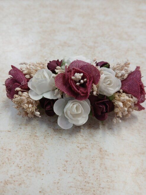 Adorno floral burdeos y blanco con pequeñas flores y follaje sobre un fondo de textura ligera.