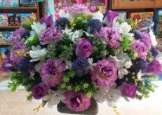 Un gran ramo de flores moradas, blancas y rosas en un jarrón sobre una mesa.