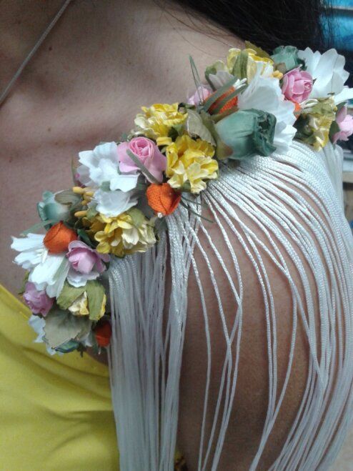 Corona floral con flores rosas, amarillas y blancas sobre un largo fleco blanco sobre una parte superior amarilla.