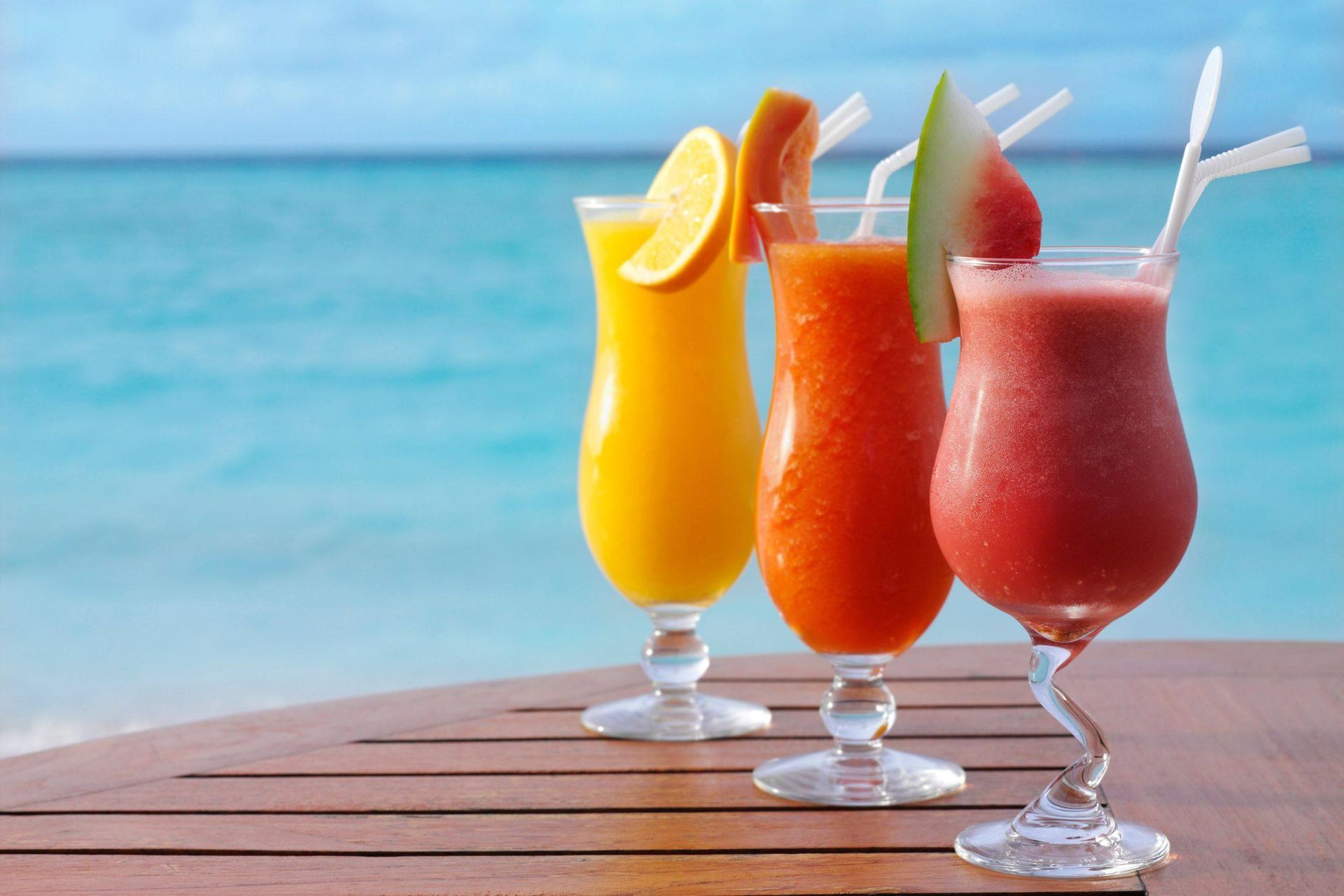 Tres bebidas en una mesa con el océano de fondo.