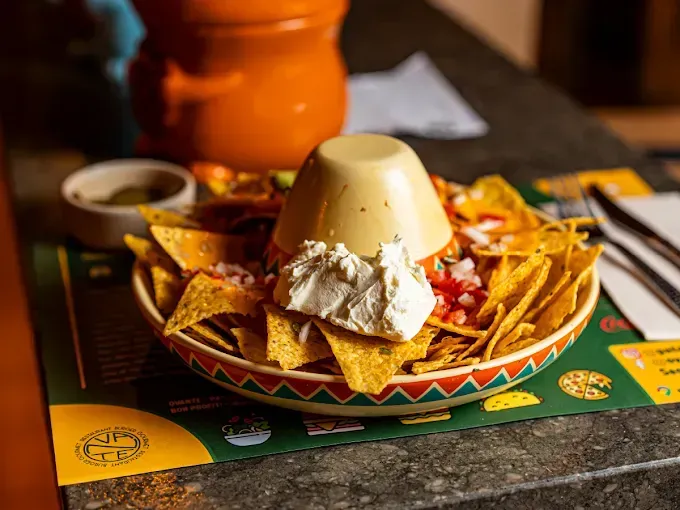 Un tazón de nachos con queso y salsa en una mesa.