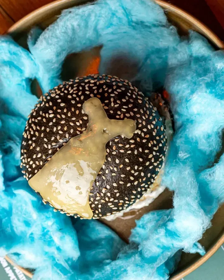 Una hamburguesa con una cruz está rodeada de algodón de azúcar azul.