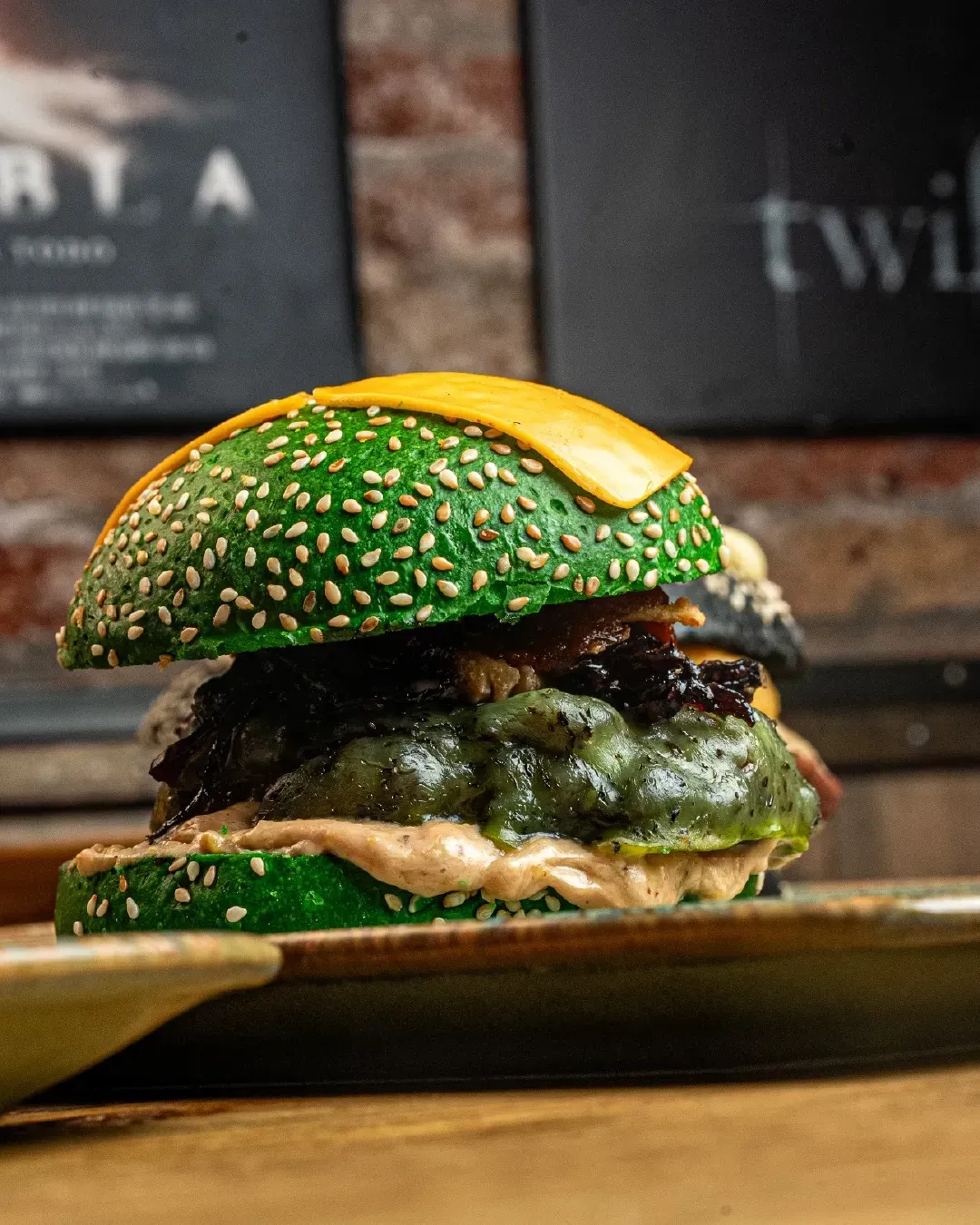Una hamburguesa verde con queso encima está en un plato sobre una mesa.