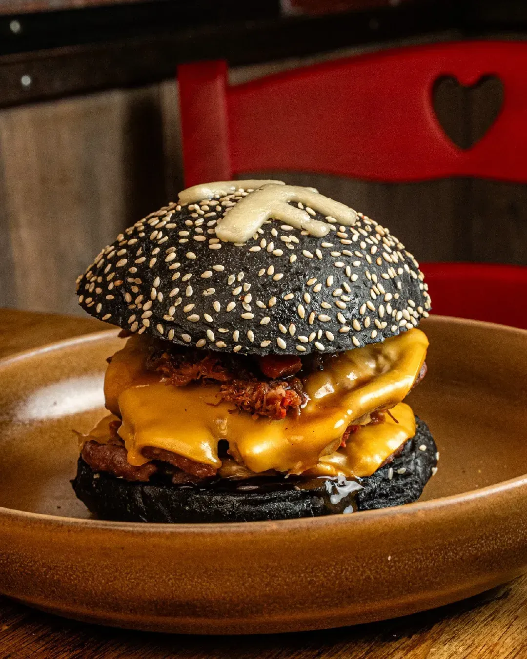 Una hamburguesa con pan negro y queso en un plato.