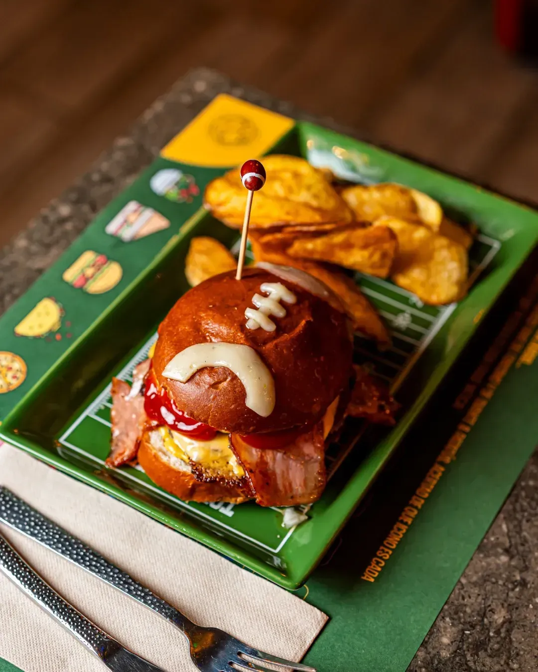 Una hamburguesa con un balón de fútbol encima está en un plato con patatas fritas.